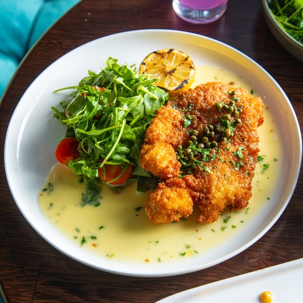 Crispy fried chicken cutlet with capers, lemon, and a side salad with cherry tomatoes.